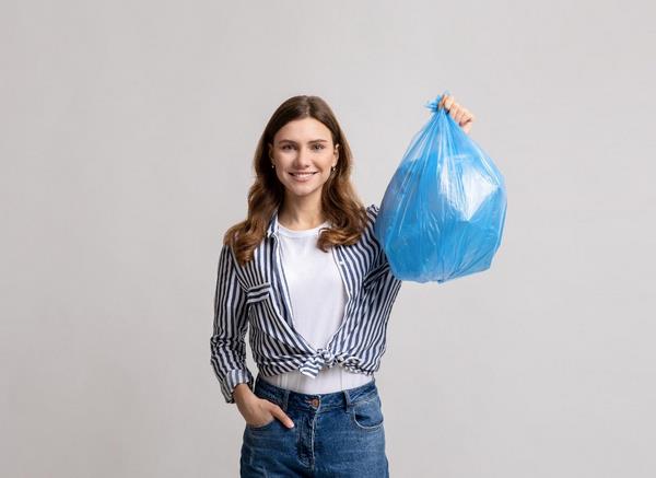 На фото – девушка держит в руке синий пакет с отходами